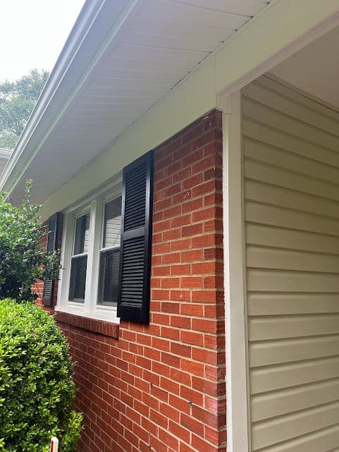 Brick and siding home exterior with black shutters and well-maintained landscaping.