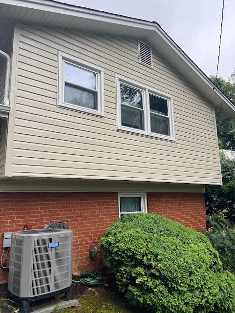 Side view of a house featuring vinyl siding, two windows, and a green shrub.