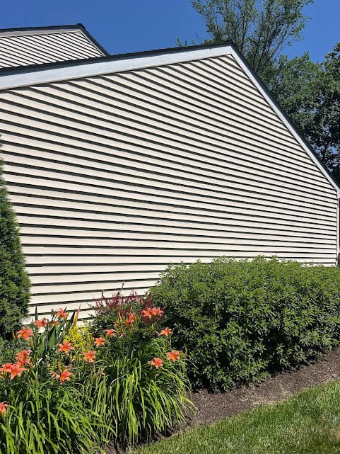 Siding on a house with vibrant flowers and green shrubs under a clear blue sky.