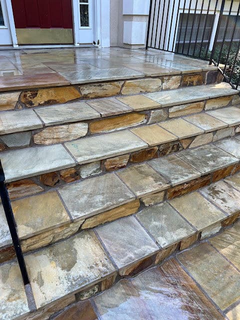 Natural stone steps leading up to a front door with a red entrance and railings.