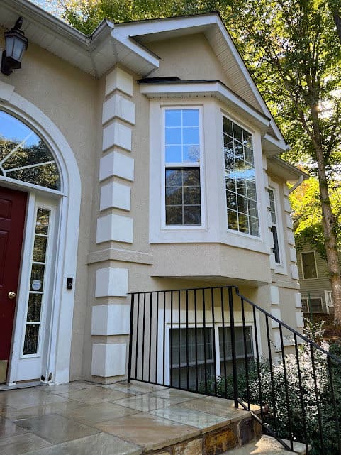 Modern home exterior with large bay windows, stone steps, and decorative railings.