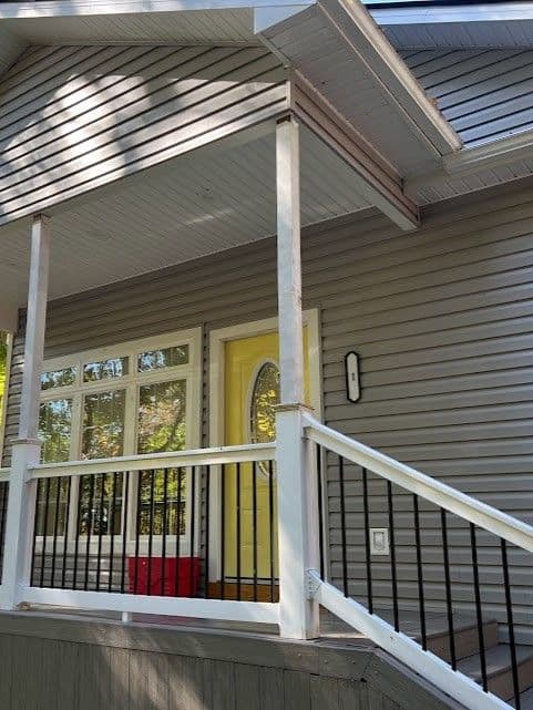 Front porch of a modern house with gray siding and yellow door, featuring white railings.