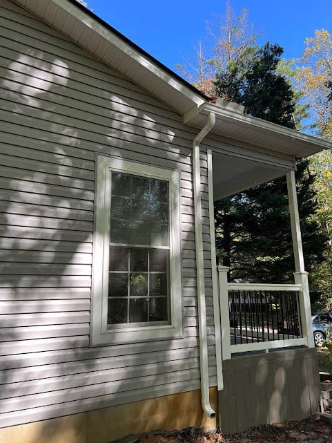 Side view of a house highlighting a window, porch, and nearby trees in sunny weather.