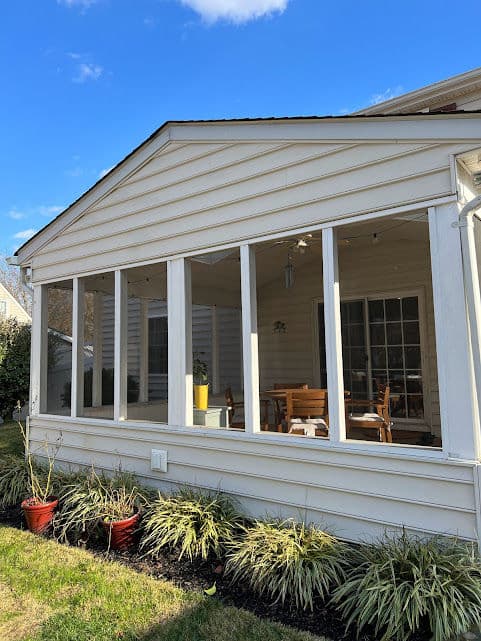 Sunroom addition with large windows, wooden furniture, and landscaped garden outside.