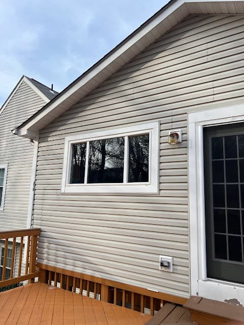 Exterior view of a house with a large window and a wooden deck, showcasing modern siding.