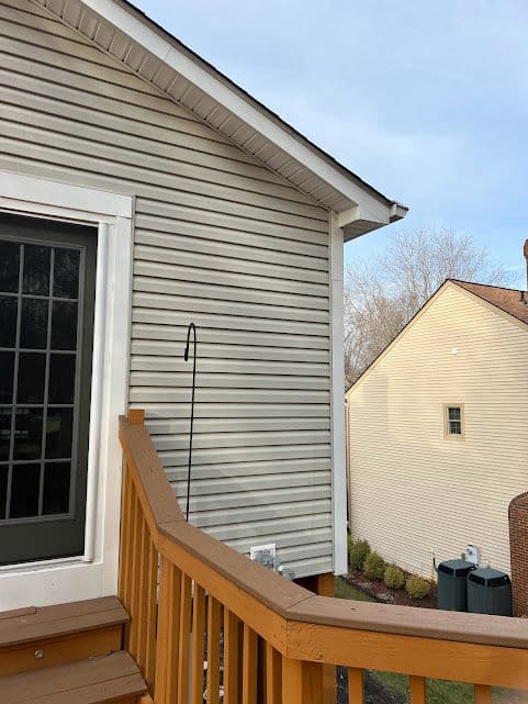 Exterior view of a house with vinyl siding and wooden deck railing on a sunny day.