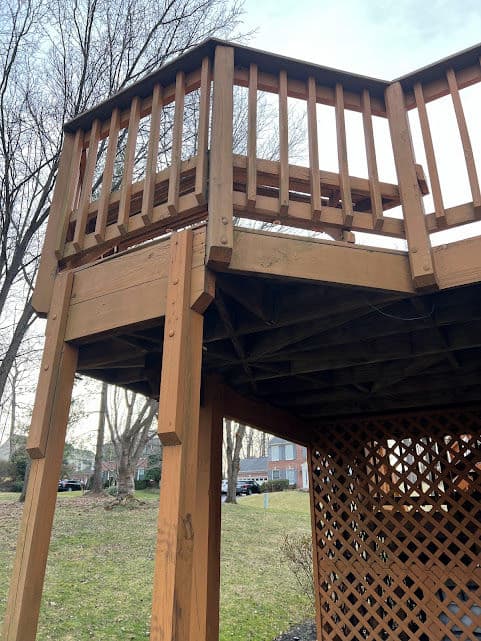 Wooden deck with railing, showcasing support beams and lattice underneath, in residential area.