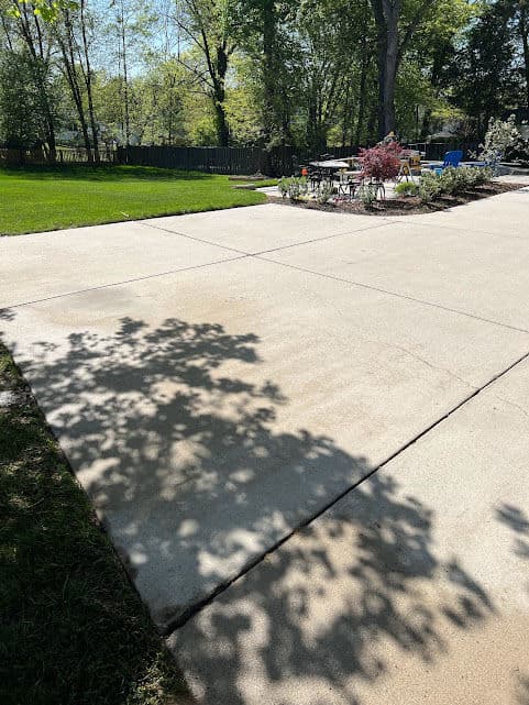 Concrete driveway with shadows from surrounding trees and landscaped garden area in sunlight.
